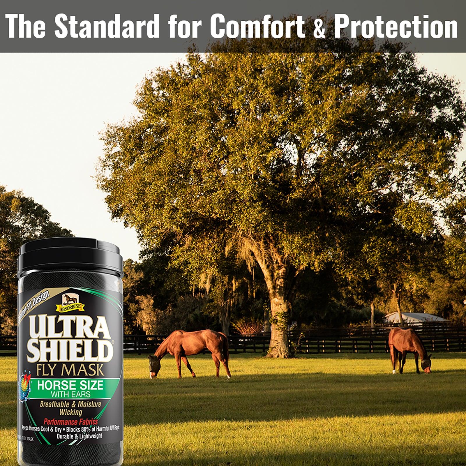 Two horses wearing fly masks in a green field with a beach tree and horse coral in the backdrop.  UltraShield fly masks, the standard for comfort & protection.