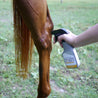 Woman's hand holding a sprayer bottle of Silver Honey Rapid Wound Repair Gel.  She is getting ready to spray it on an open wound on a horses leg.